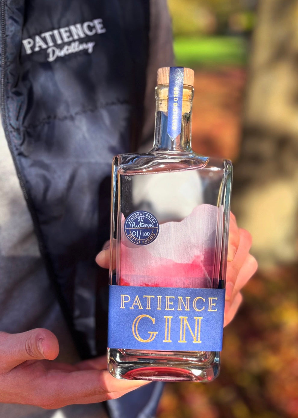 Person holding a bottle of Patience Autumn Gin with a blurred background