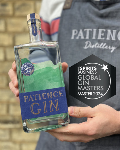 Bottle of Patience Spring Gin held by a person wearing a branded apron with a badge for 'Spirits Business Global Gin Masters Master 2024'.